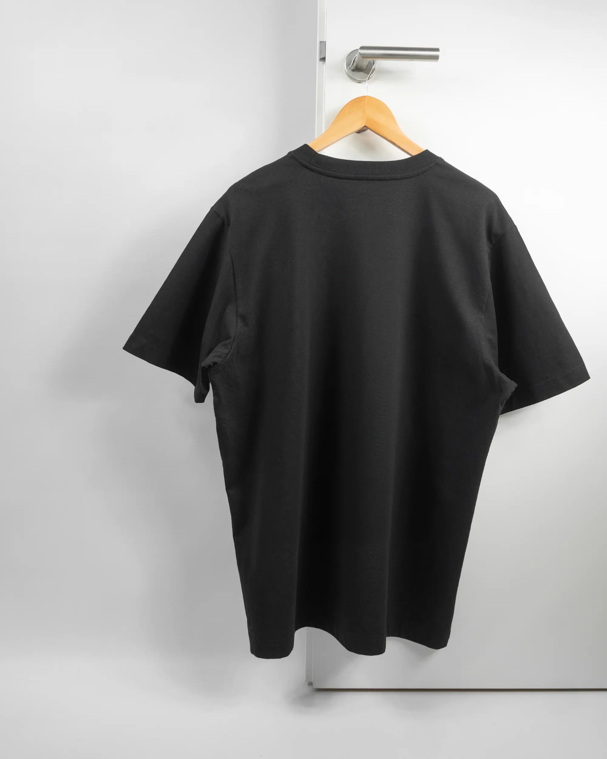 Rückseite des Organic Unisex T-Shirt Heavy Oversized von Maondo ohne Motiv in der Farbe Black und in der Größe L auf einem Bügel an der Türklinke aufgehängt