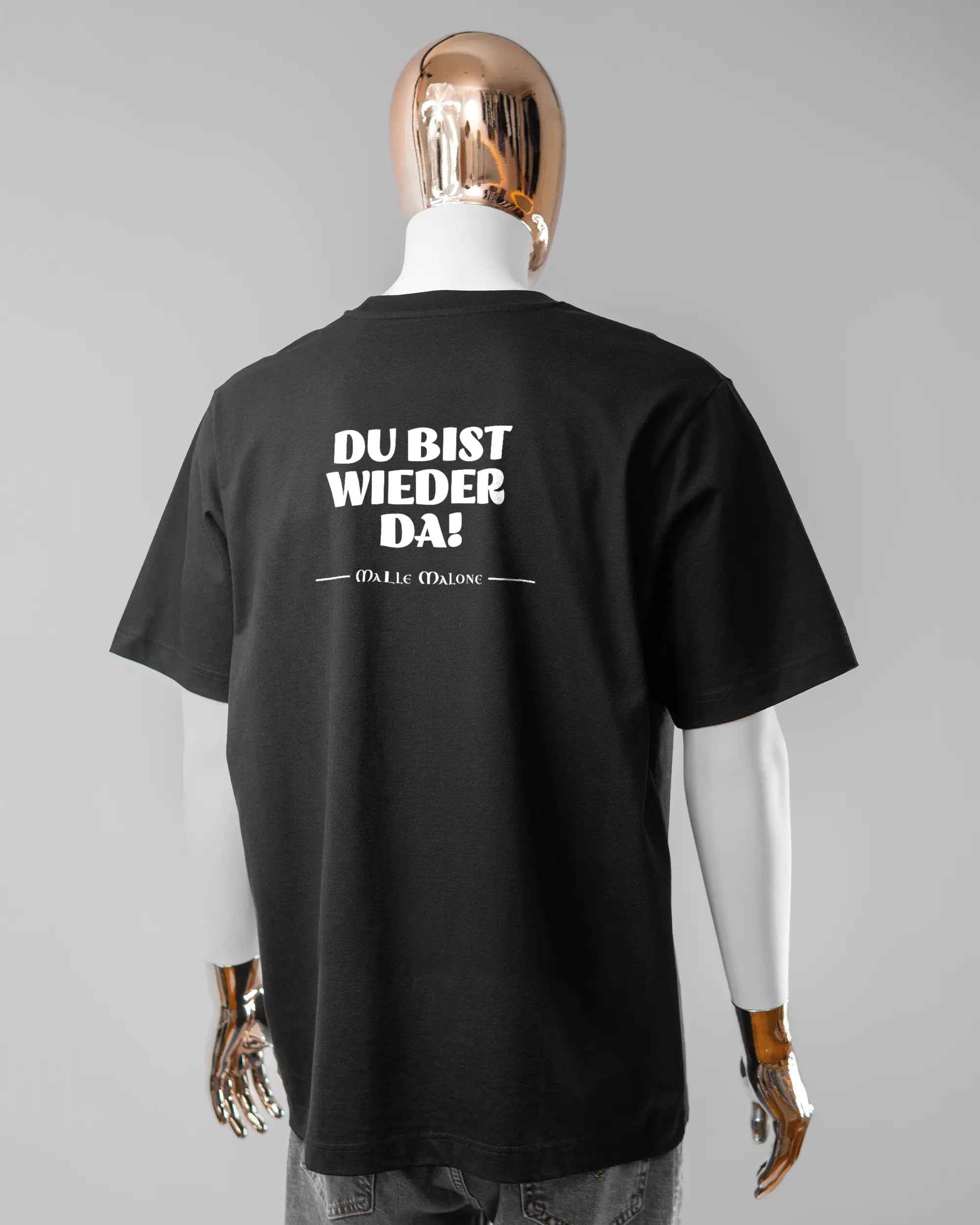 Rückseite des Organic Unisex T-Shirt Heavy Oversized von Maondo mit dem Design Wieder da in der Farbe Black und in der Größe L getragen von einer maskulinen Puppe