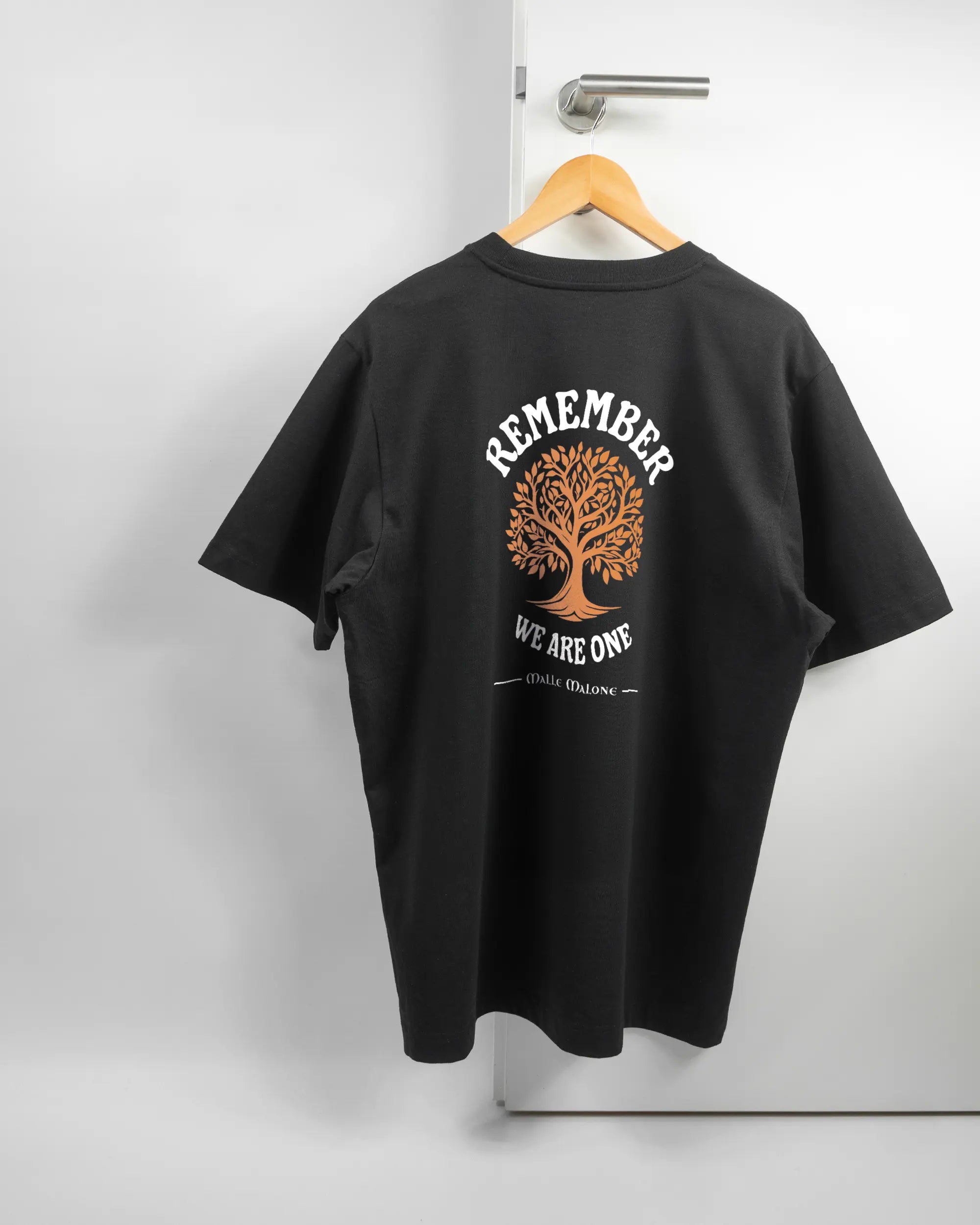 Rückseite des Organic Unisex T-Shirt Heavy Oversized von Maondo mit dem Design We are one in der Farbe Black und in der Größe L auf einem Bügel an der Türklinke aufgehängt