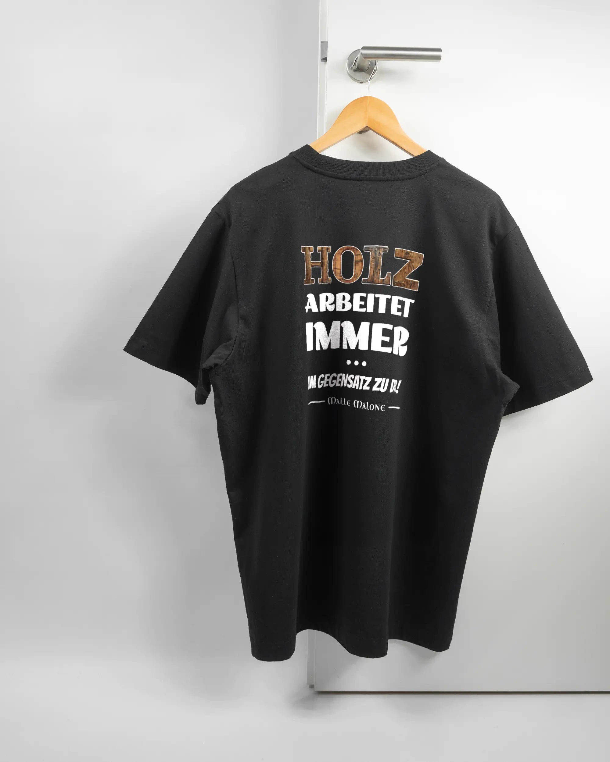 Rückseite des Organic Unisex T-Shirt Heavy Oversized von Maondo mit dem Design Holzarbeit in der Farbe Black und in der Größe L auf einem Bügel an der Türklinke aufgehängt