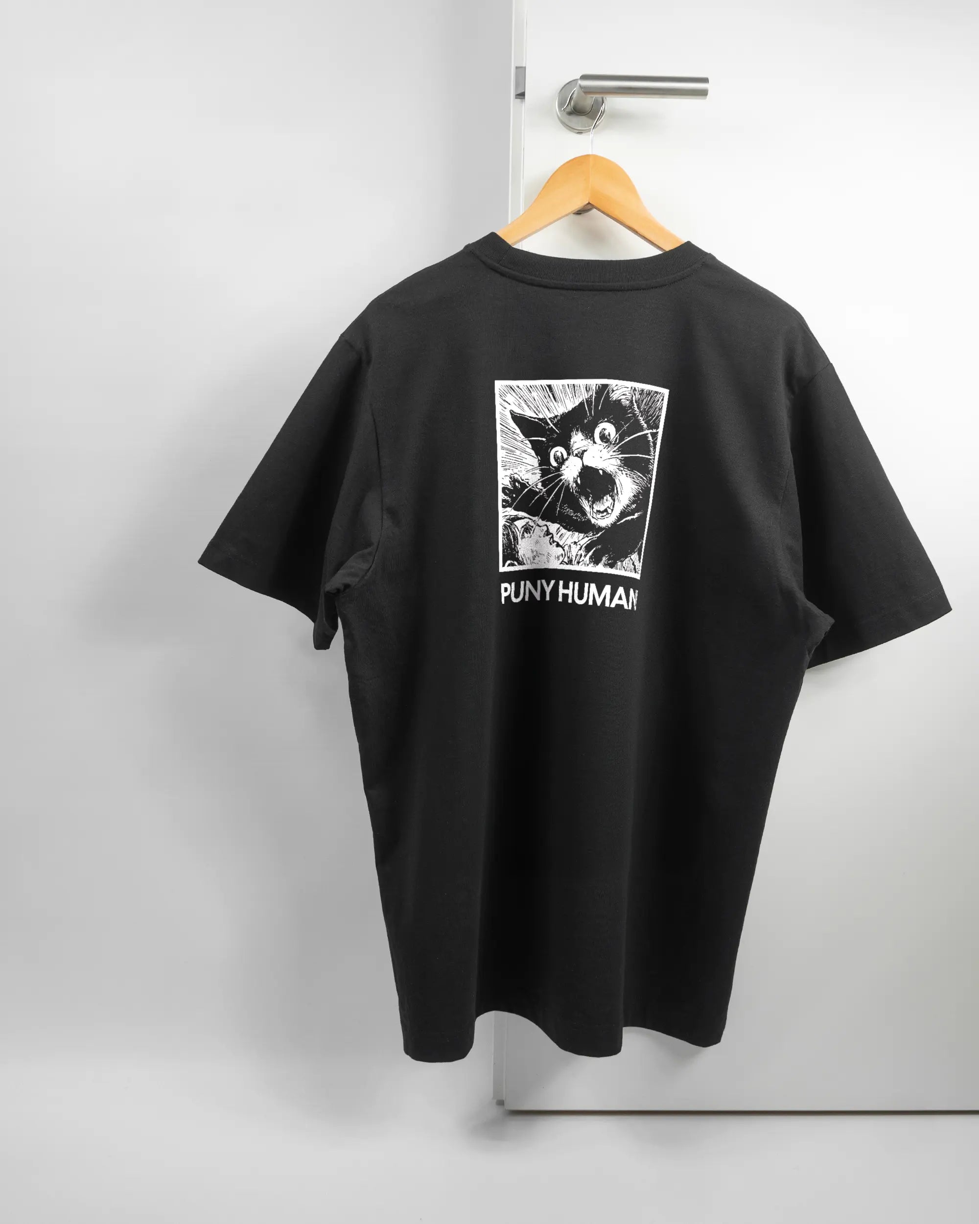 Rückseite des Organic Unisex T-Shirt Heavy Oversized von Maondo mit dem Design Puny Human in der Farbe Black und in der Größe L auf einem Bügel an der Türklinke aufgehängt