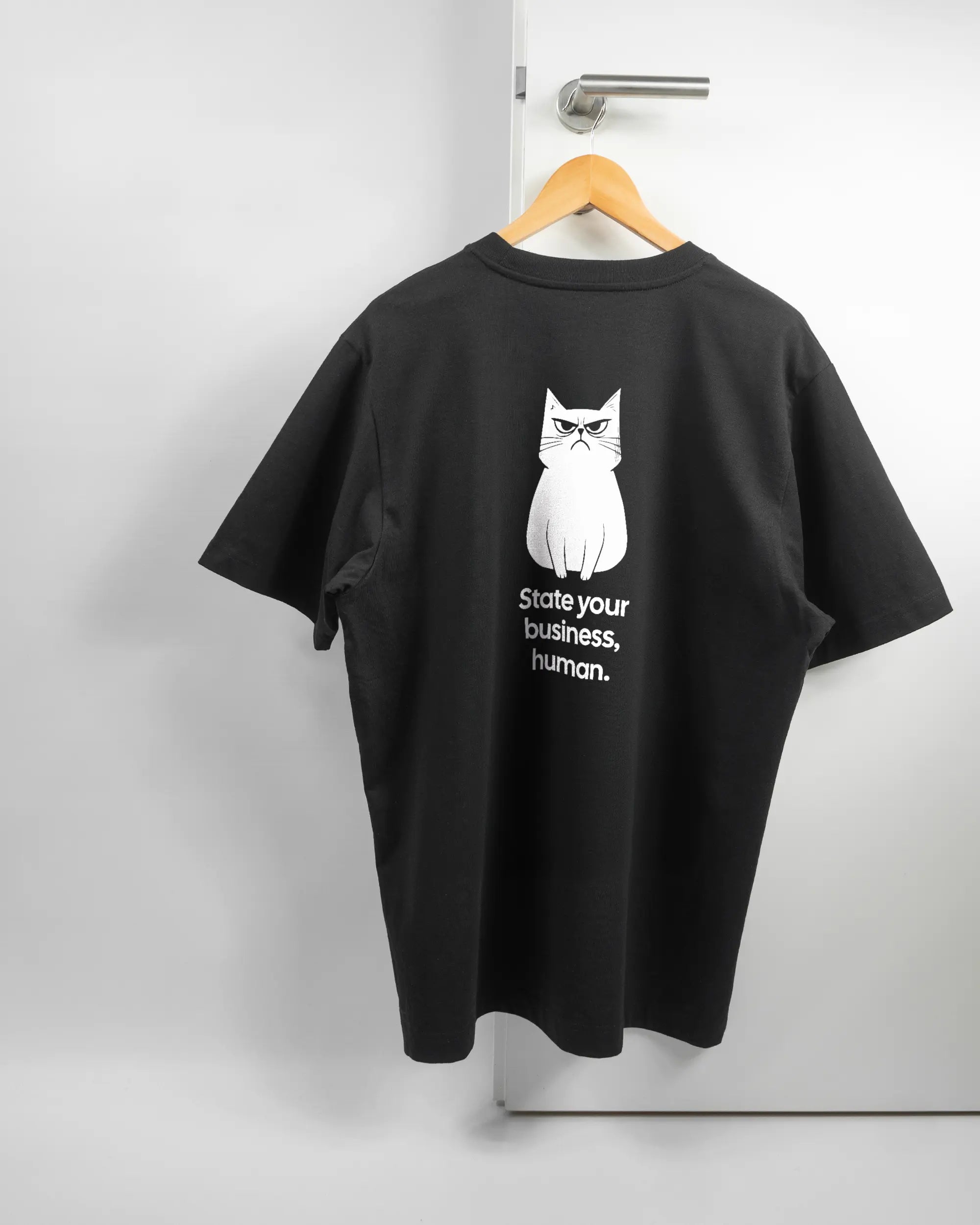 Rückseite des Organic Unisex T-Shirt Heavy Oversized von Maondo mit dem Design Grumpy Purr in der Farbe Black und in der Größe L auf einem Bügel an der Türklinke aufgehängt