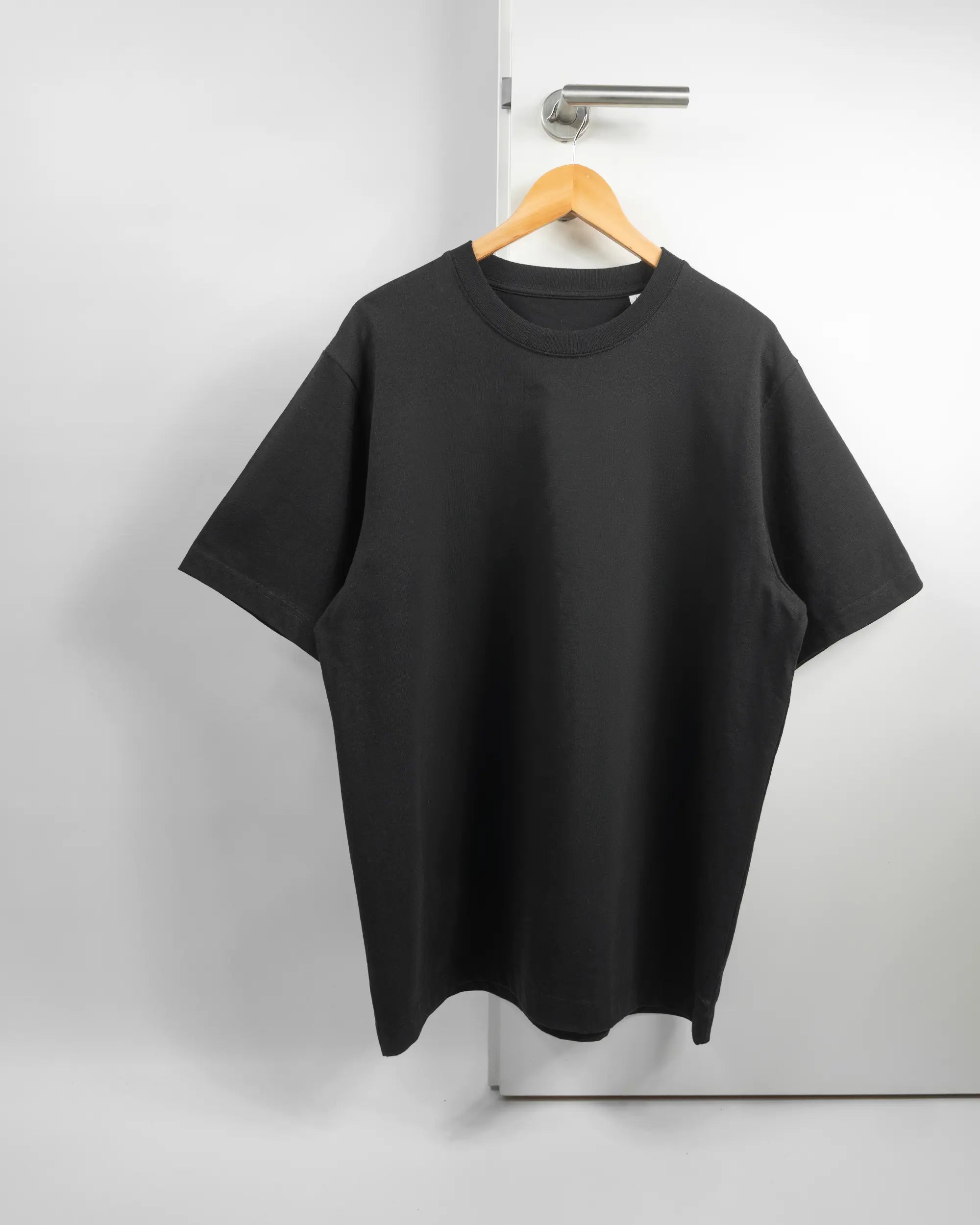 Vorderseite des Organic Unisex T-Shirt Heavy Oversized von Maondo ohne Motiv in der Farbe Black und in der Größe L auf einem Bügel an der Türklinke aufgehängt