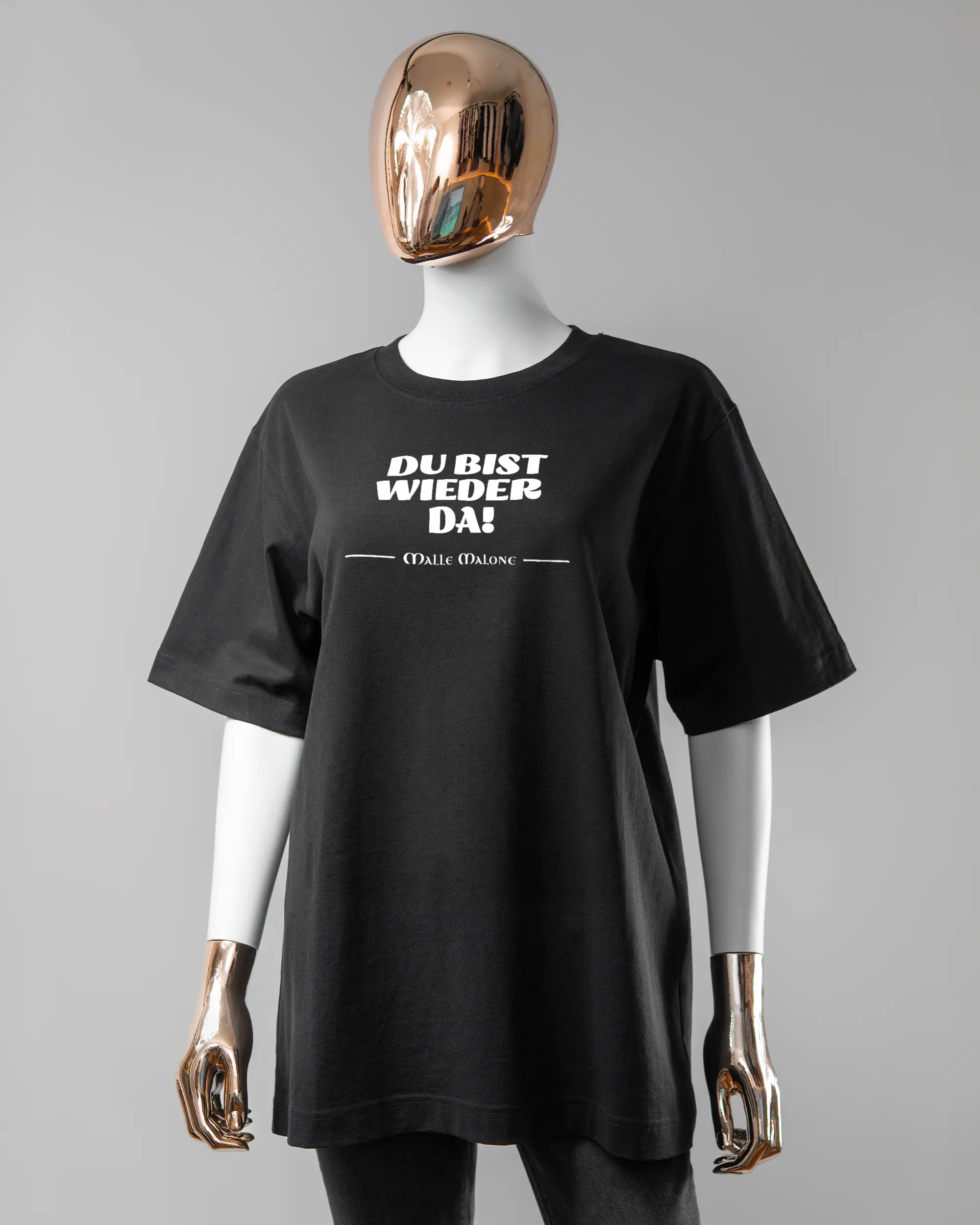 Vorderseite des Organic Unisex T-Shirt Heavy Oversized von Maondo mit dem Design Wieder da in der Farbe Black und in der Größe S getragen von einer femininen Puppe