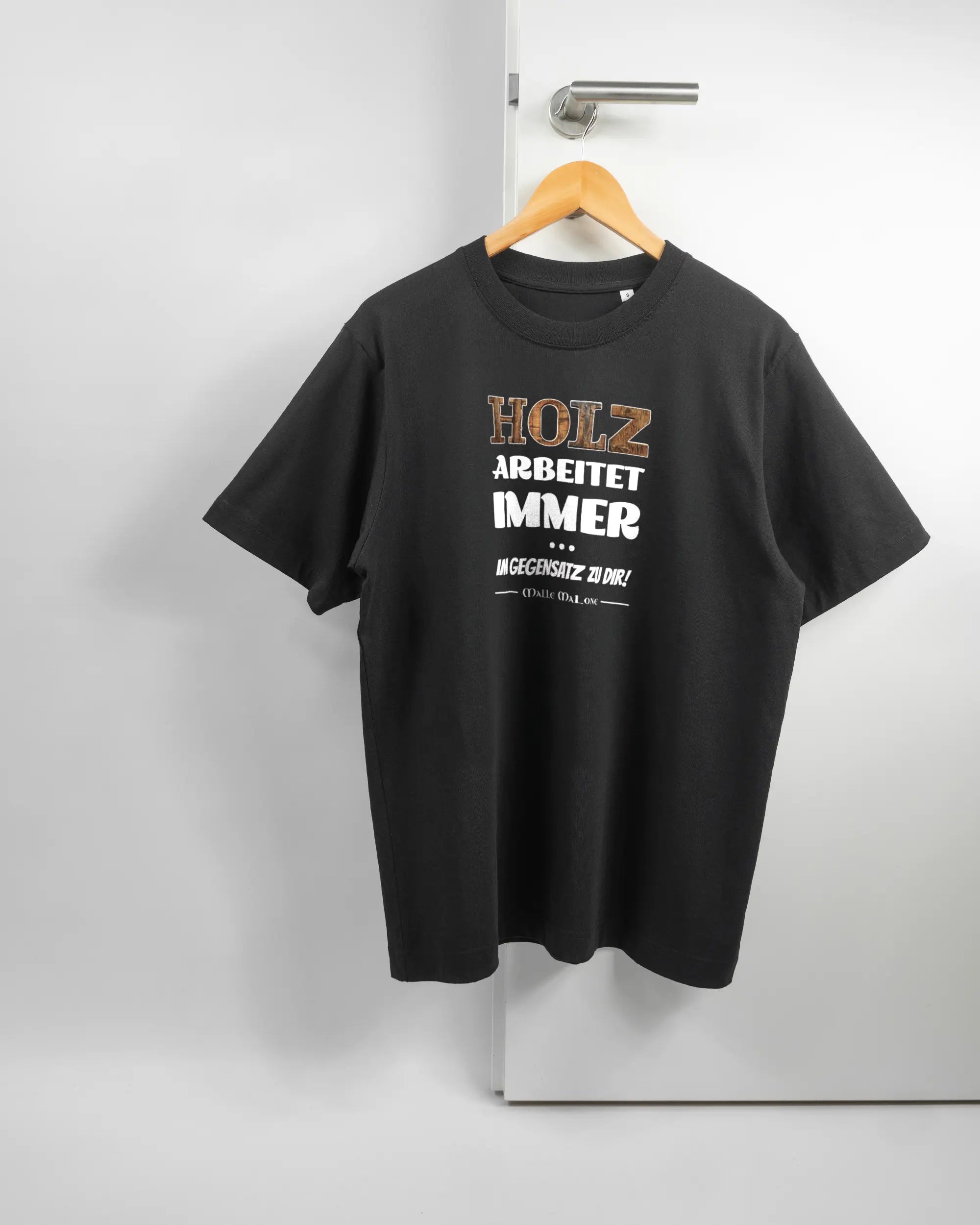 Vorderseite des Organic Unisex T-Shirt Heavy Oversized von Maondo mit dem Design Holzarbeit in der Farbe Black und in der Größe S auf einem Bügel an der Türklinke aufgehängt