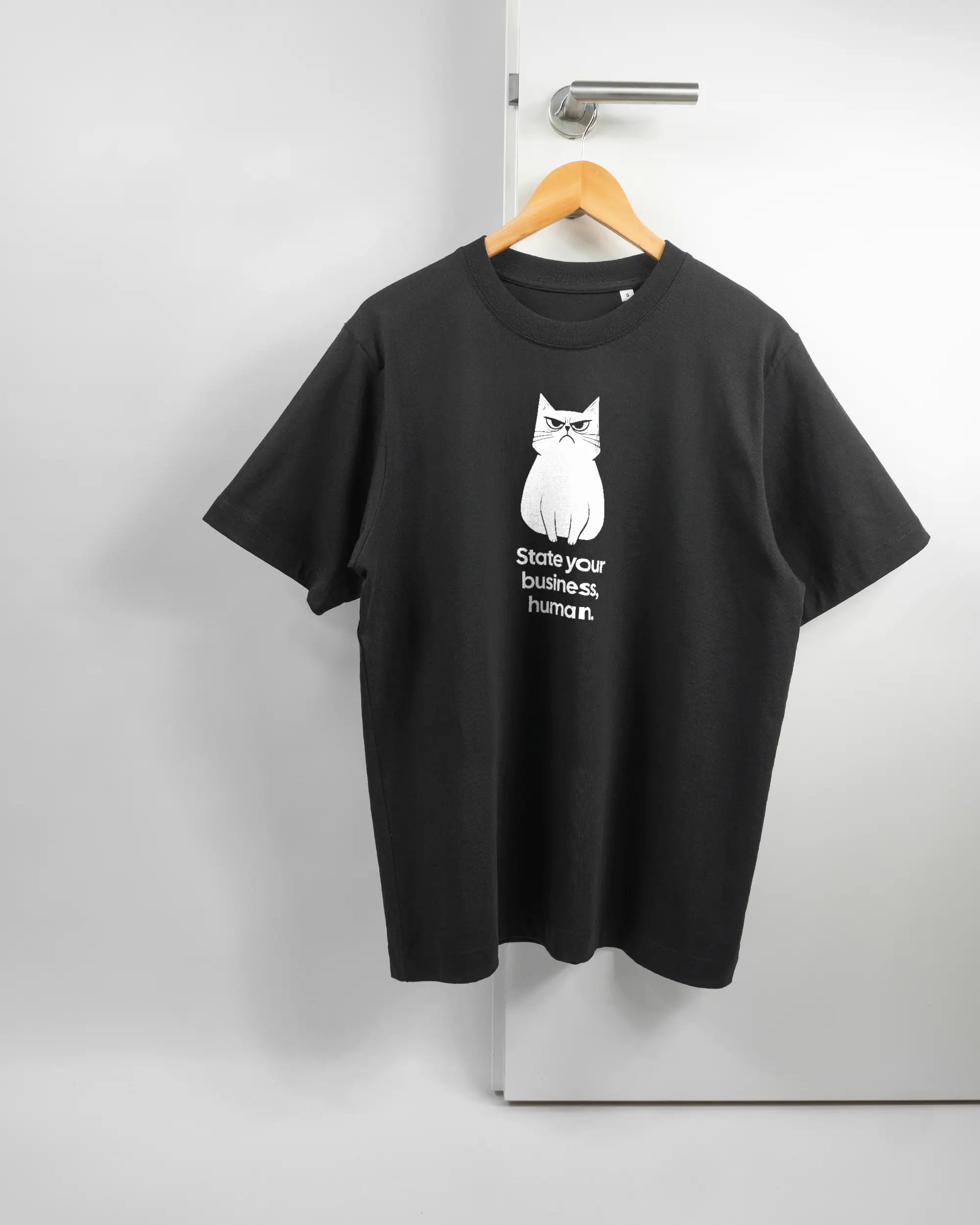 Vorderseite des Organic Unisex T-Shirt Heavy Oversized von Maondo mit dem Design Grumpy Purr in der Farbe Black und in der Größe S auf einem Bügel an der Türklinke aufgehängt