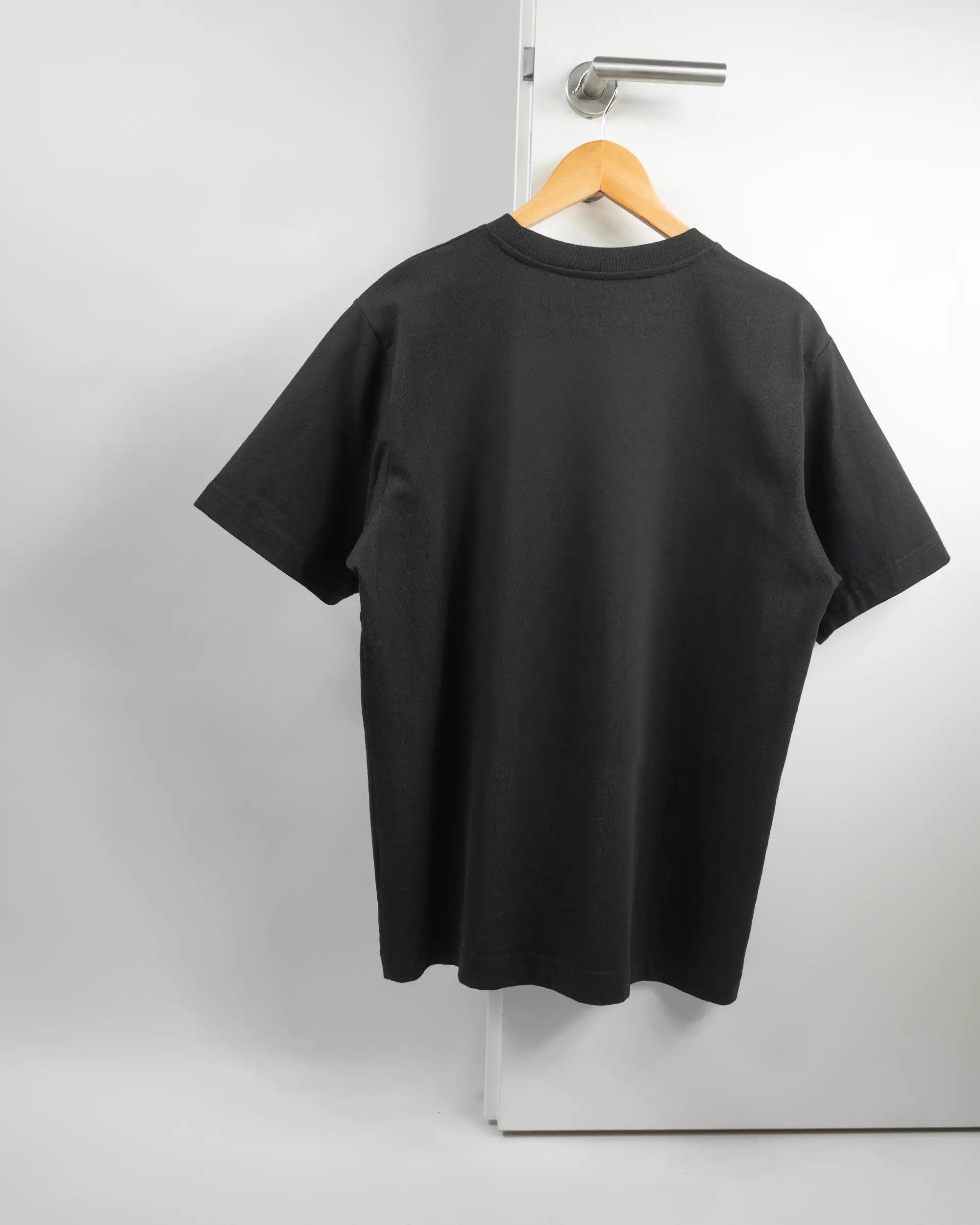 Rückseite des Organic Unisex T-Shirt Heavy Oversized von Maondo ohne Motiv in der Farbe Black und in der Größe S auf einem Bügel an der Türklinke aufgehängt