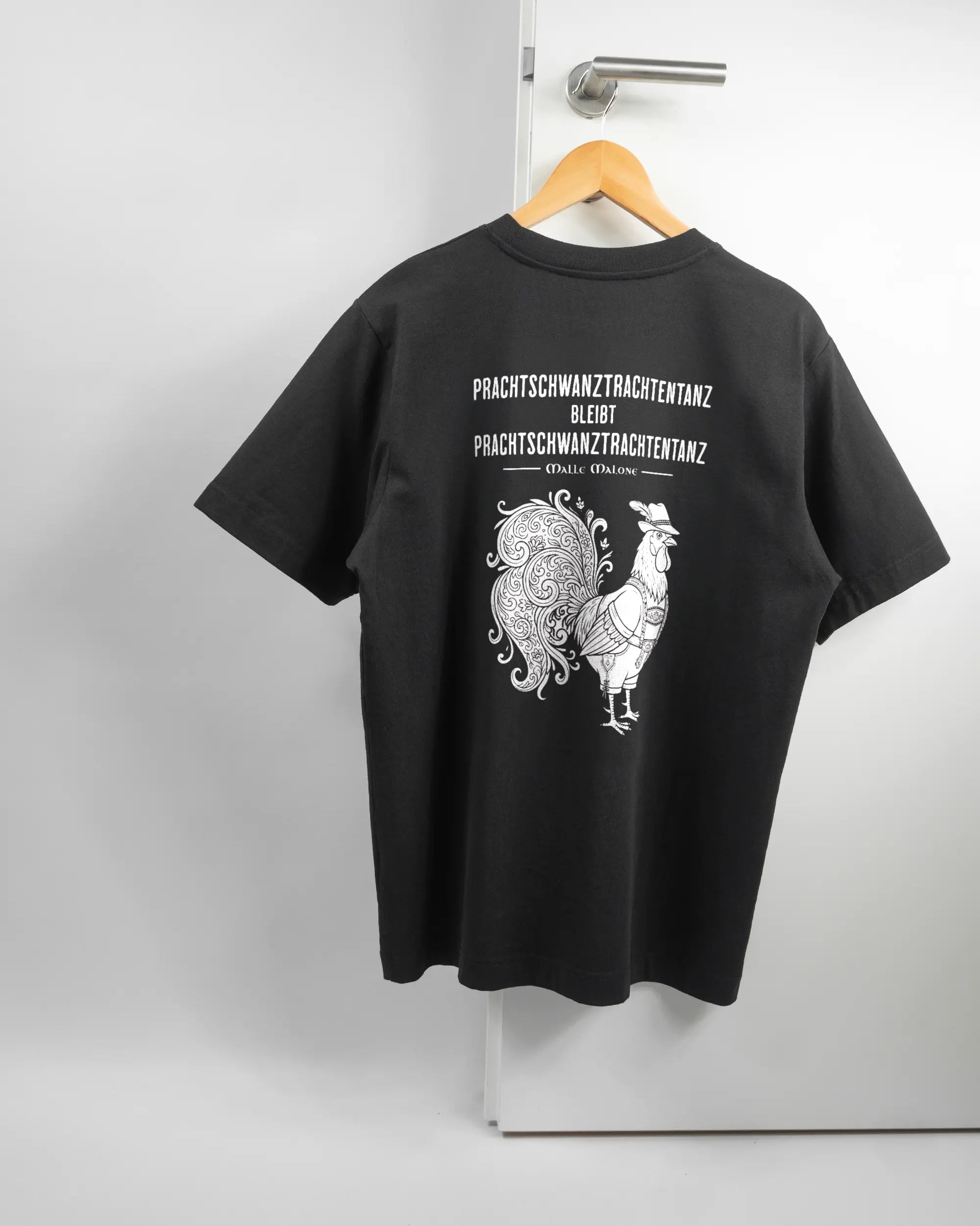Rückseite des Organic Unisex T-Shirt Heavy Oversized von Maondo mit dem Design Trachtentanz in der Farbe Black und in der Größe S auf einem Bügel an der Türklinke aufgehängt