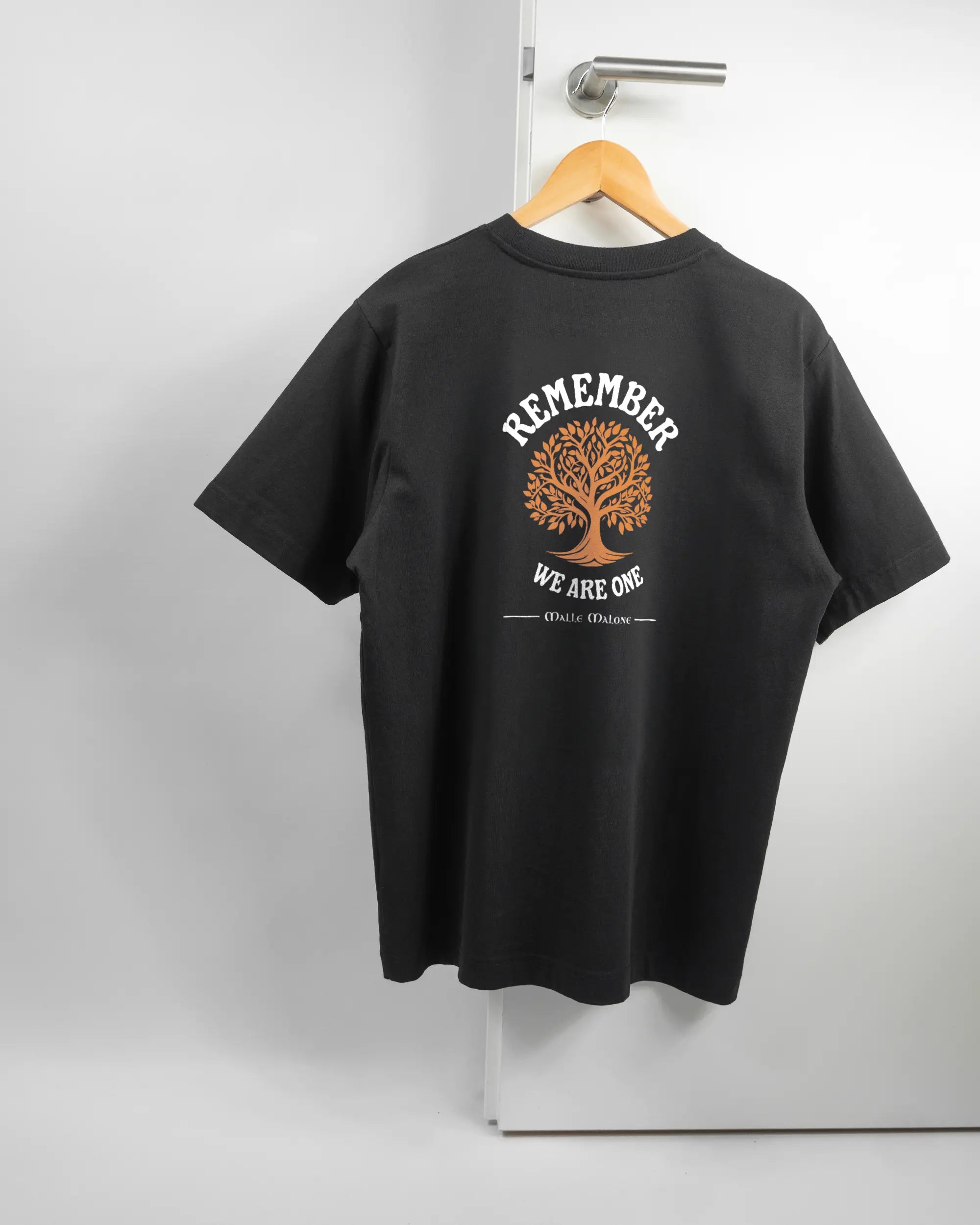 Rückseite des Organic Unisex T-Shirt Heavy Oversized von Maondo mit dem Design We are one in der Farbe Black und in der Größe S auf einem Bügel an der Türklinke aufgehängt