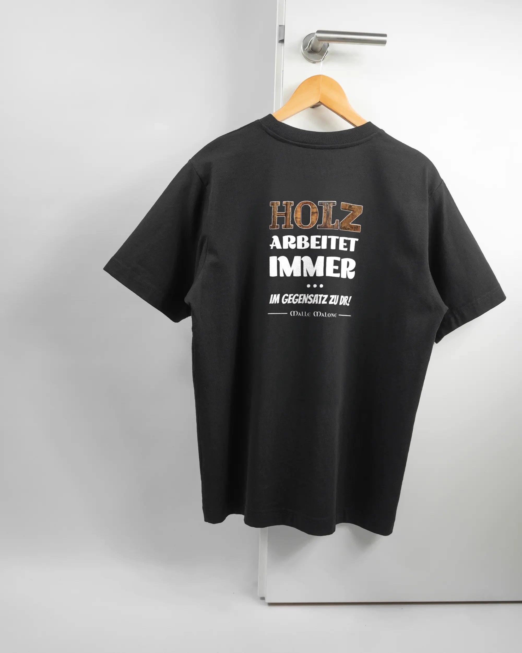 Rückseite des Organic Unisex T-Shirt Heavy Oversized von Maondo mit dem Design Holzarbeit in der Farbe Black und in der Größe S auf einem Bügel an der Türklinke aufgehängt