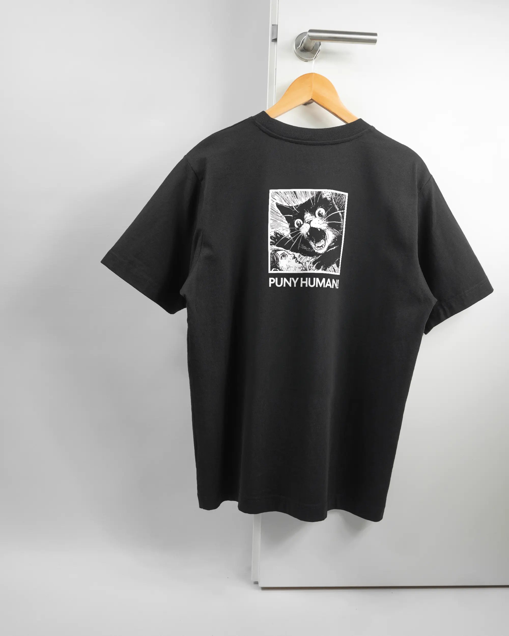 Rückseite des Organic Unisex T-Shirt Heavy Oversized von Maondo mit dem Design Puny Human in der Farbe Black und in der Größe S auf einem Bügel an der Türklinke aufgehängt