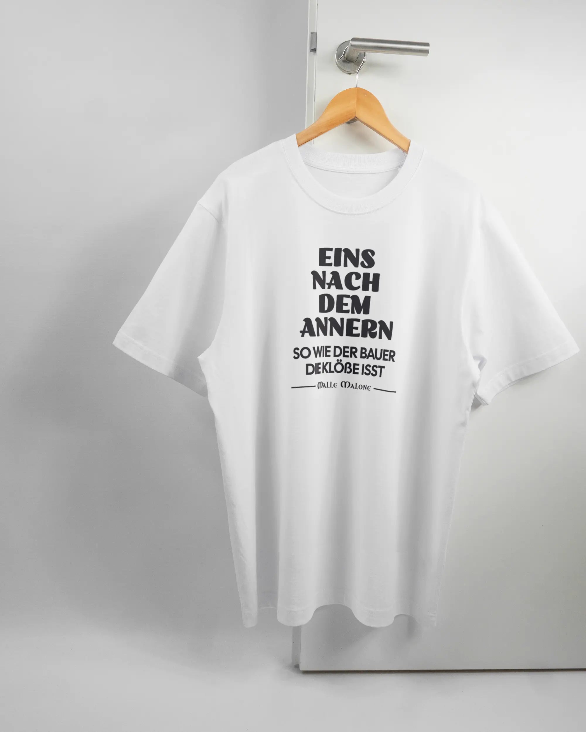 Vorderseite des Organic Unisex T-Shirt Heavy Oversized von Maondo mit dem Design Eins nach dem Annern in der Farbe White und in der Größe L auf einem Bügel an der Türklinke aufgehängt