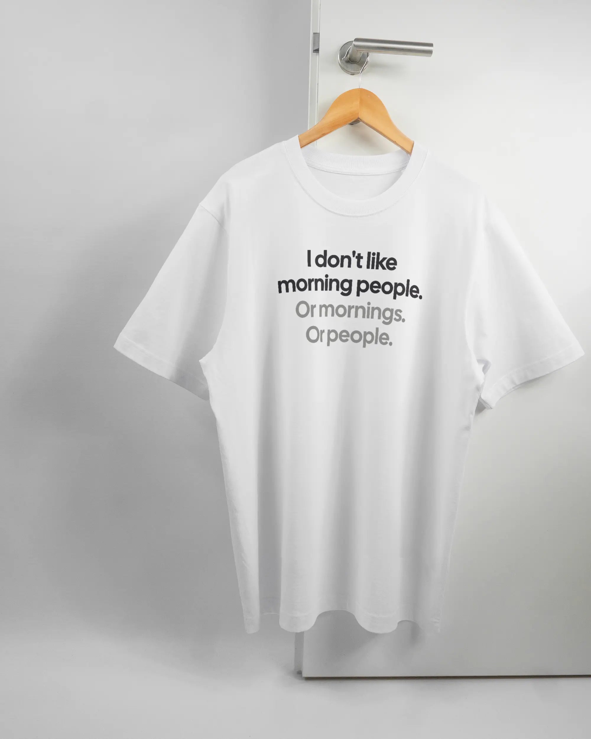 Vorderseite des Organic Unisex T-Shirt Heavy Oversized von Maondo mit dem Design Morning Person in der Farbe White und in der Größe L auf einem Bügel an der Türklinke aufgehängt