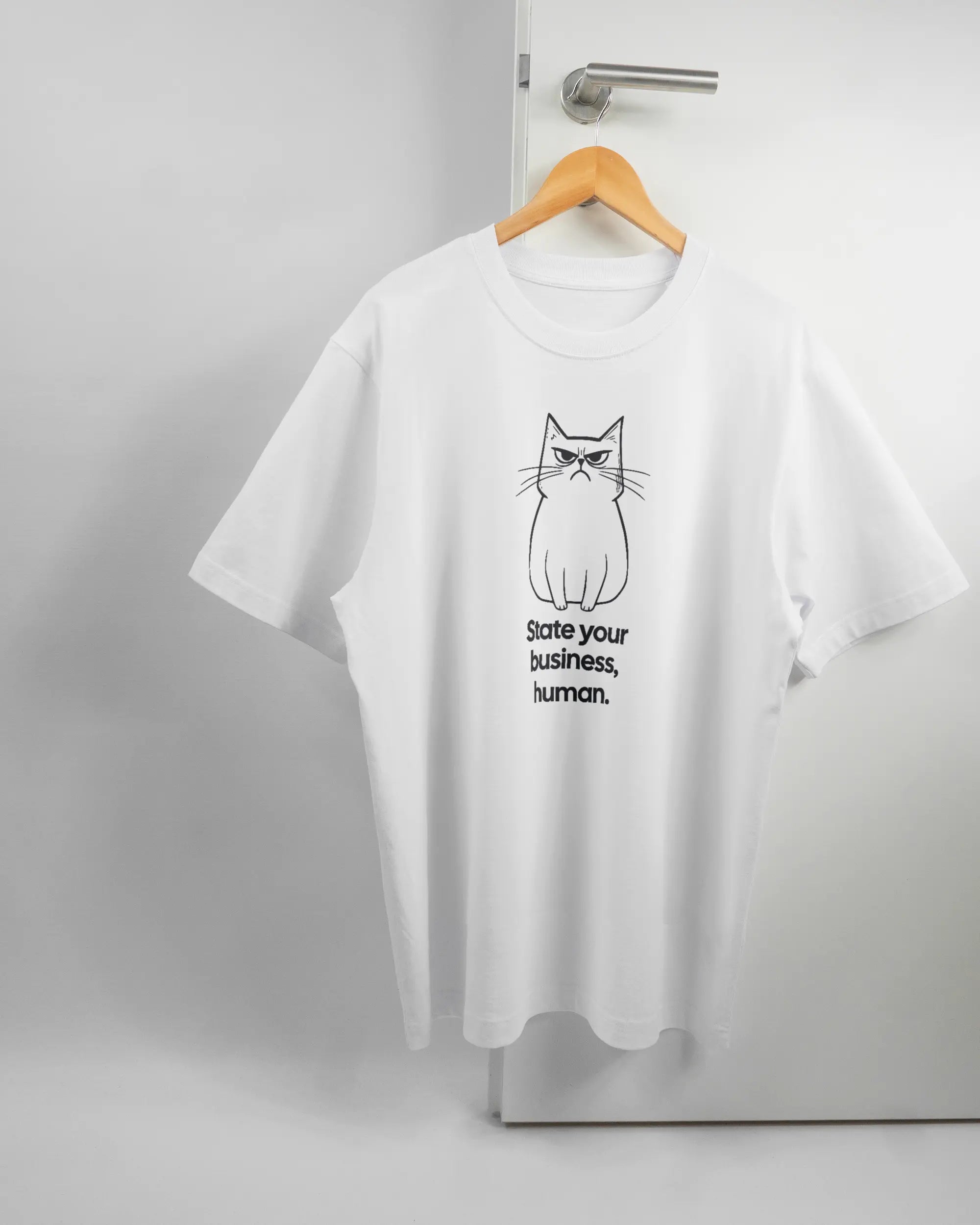 Vorderseite des Organic Unisex T-Shirt Heavy Oversized von Maondo mit dem Design Grumpy Purr in der Farbe White und in der Größe L auf einem Bügel an der Türklinke aufgehängt