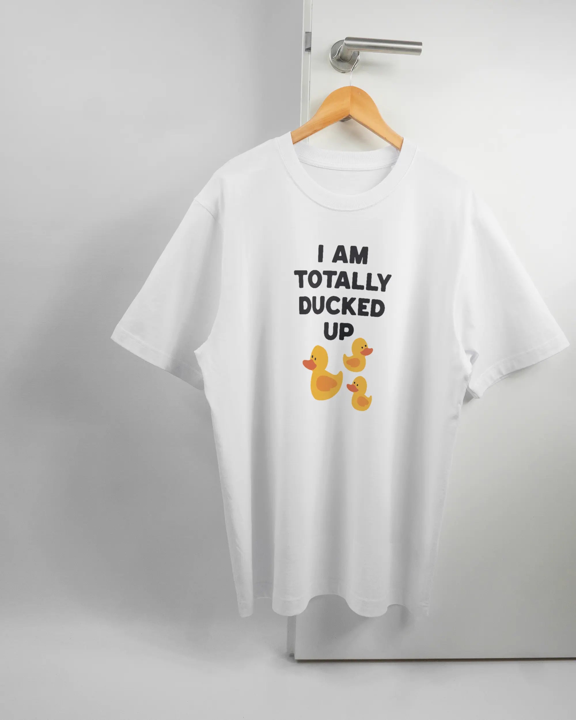 Vorderseite des Organic Unisex T-Shirt Heavy Oversized von Maondo mit dem Design Ducked Up in der Farbe White und in der Größe L auf einem Bügel an der Türklinke aufgehängt