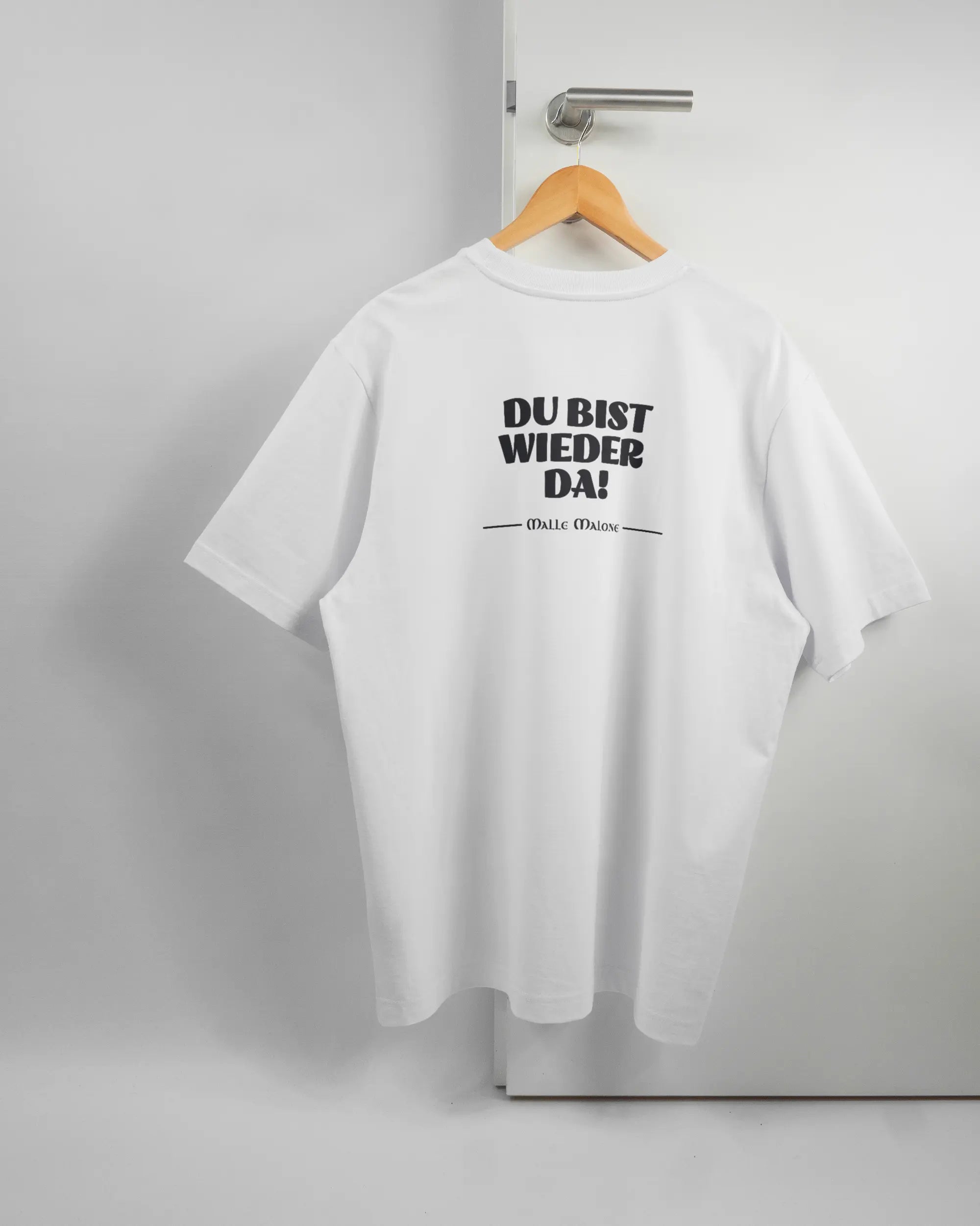 Rückseite des Organic Unisex T-Shirt Heavy Oversized von Maondo mit dem Design Wieder da in der Farbe White und in der Größe L auf einem Bügel an der Türklinke aufgehängt