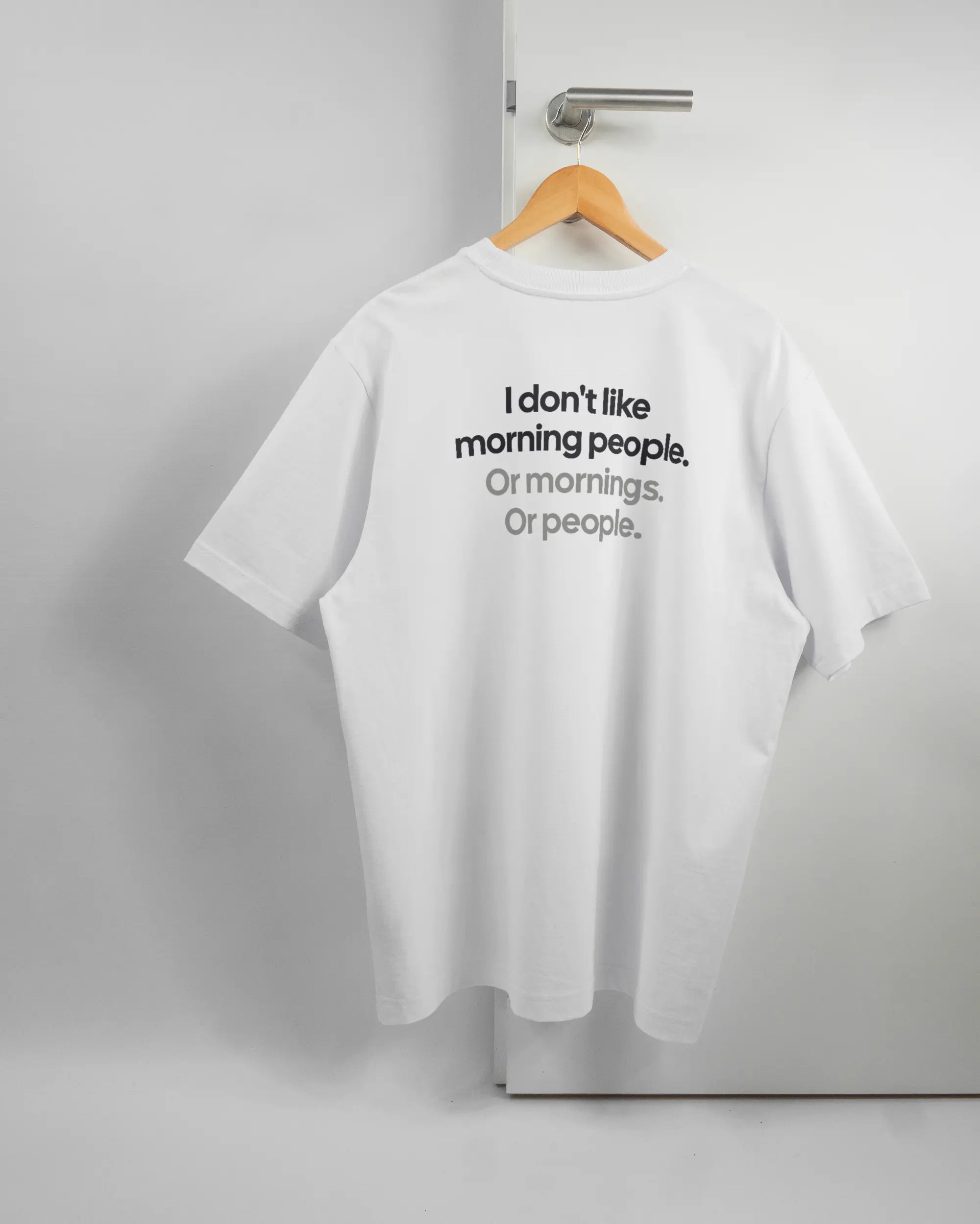 Rückseite des Organic Unisex T-Shirt Heavy Oversized von Maondo mit dem Design Morning Person in der Farbe White und in der Größe L auf einem Bügel an der Türklinke aufgehängt