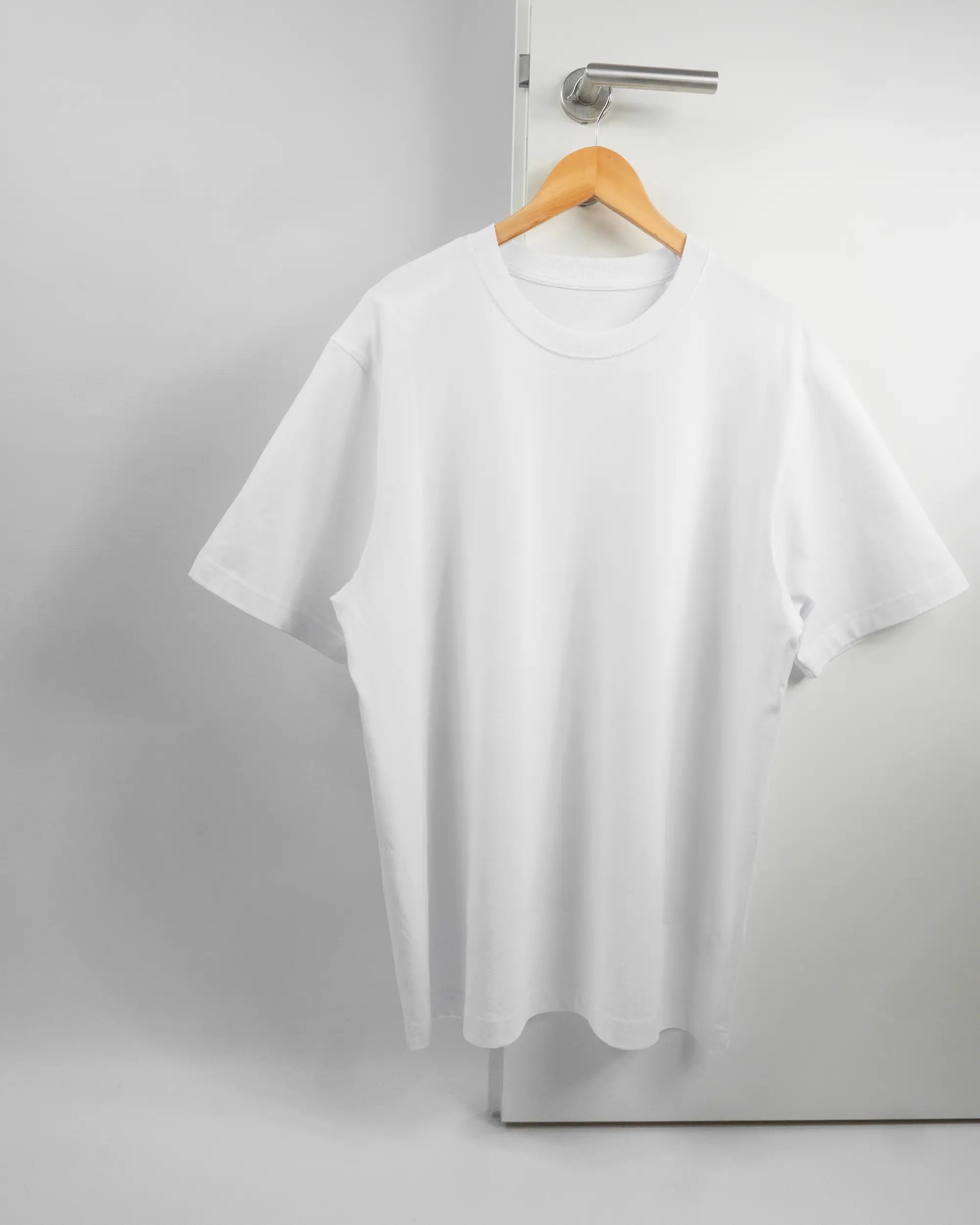 Vorderseite des Organic Unisex T-Shirt Heavy Oversized von Maondo ohne Motiv in der Farbe White und in der Größe L auf einem Bügel an der Türklinke aufgehängt