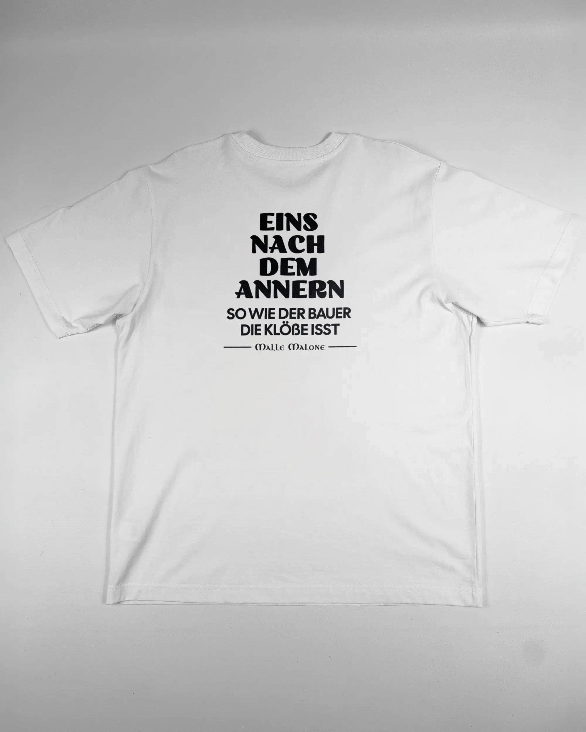 Rückseite des Organic Unisex T-Shirt Heavy Oversized von Maondo mit dem Design Eins nach dem Annern in der Farbe White und in der Größe L flach auf den Boden gelegt