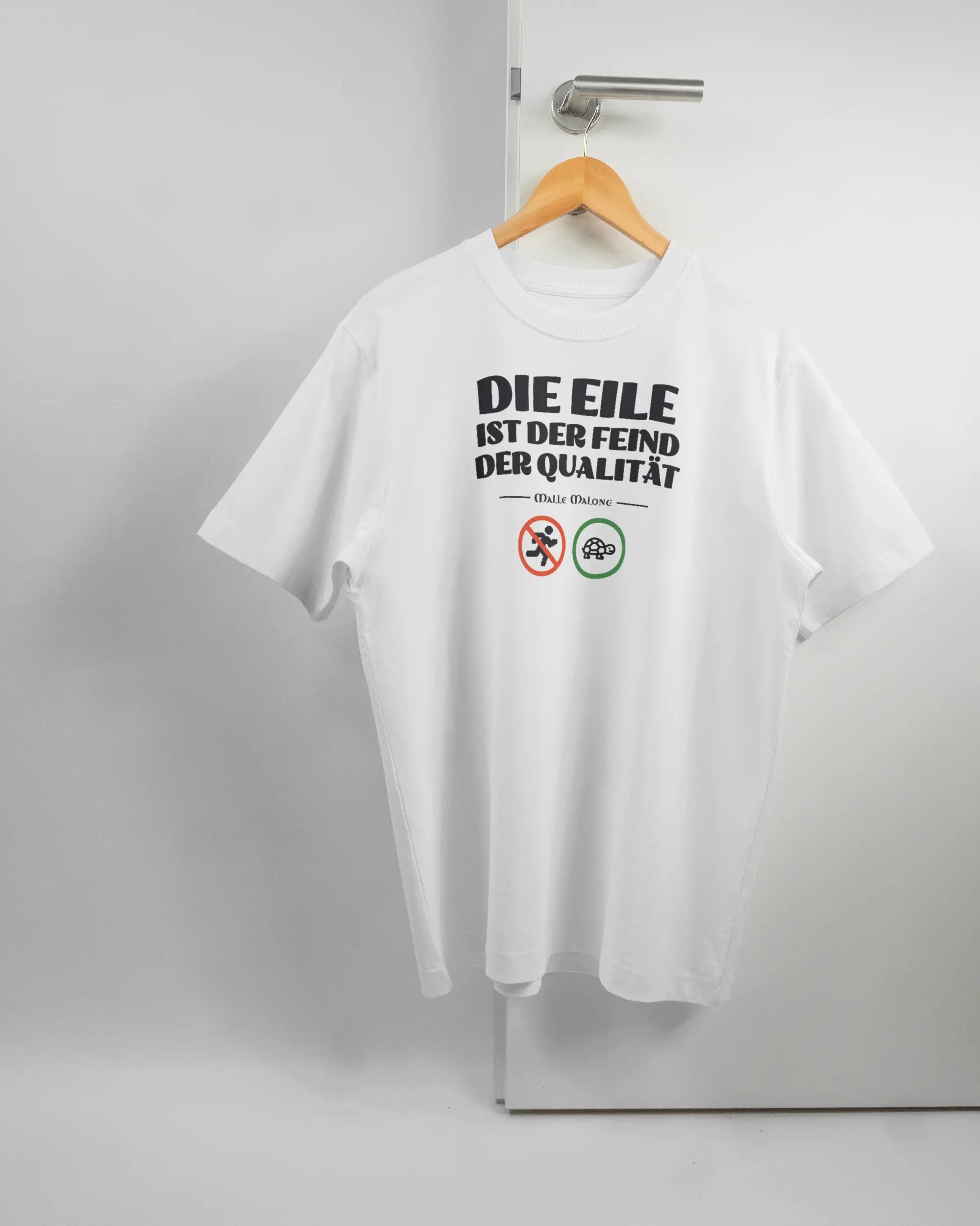 Vorderseite des Organic Unisex T-Shirt Heavy Oversized von Maondo mit dem Design Keine Eile in der Farbe White und in der Größe S auf einem Bügel an der Türklinke aufgehängt