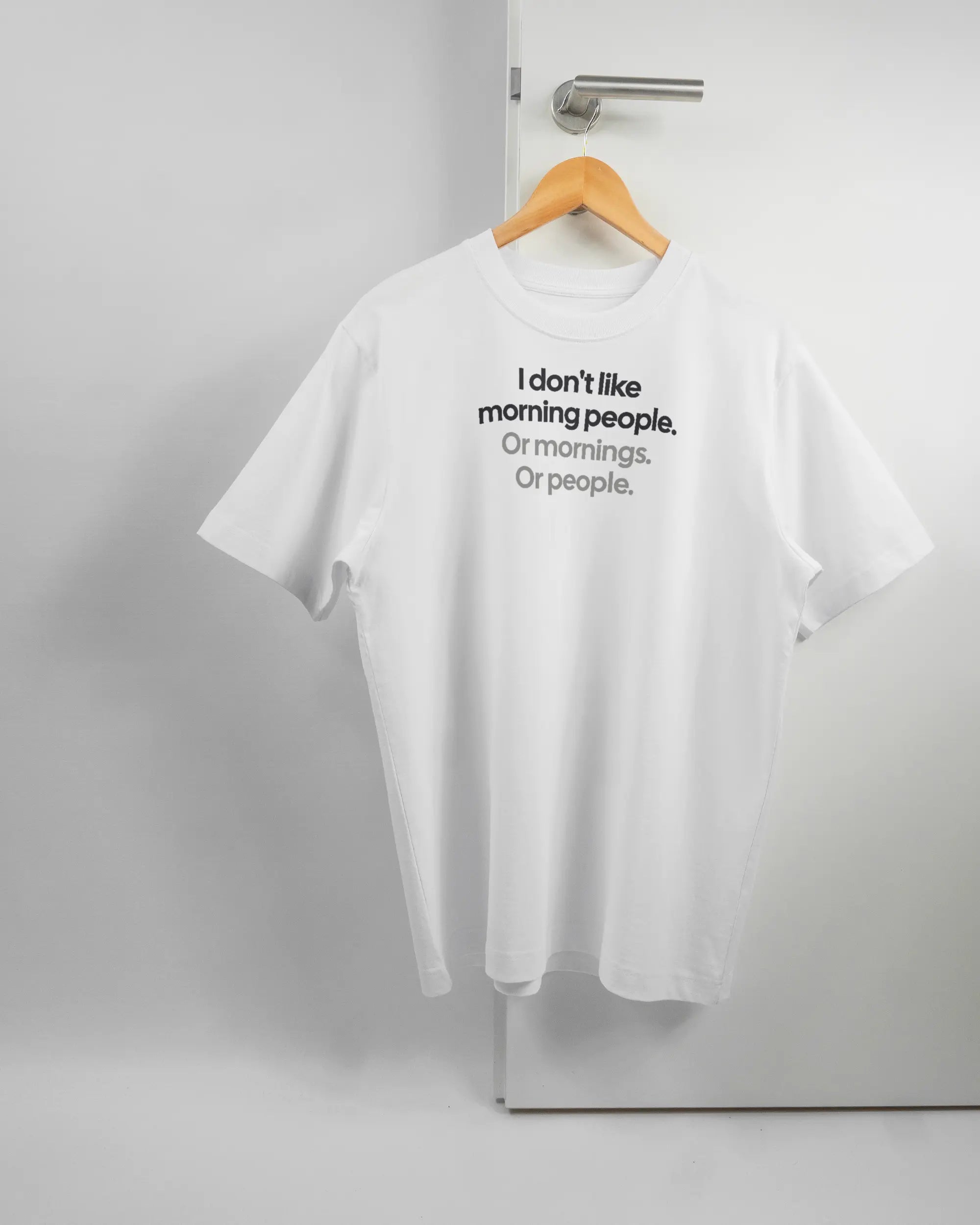 Vorderseite des Organic Unisex T-Shirt Heavy Oversized von Maondo mit dem Design Morning Person in der Farbe White und in der Größe S auf einem Bügel an der Türklinke aufgehängt