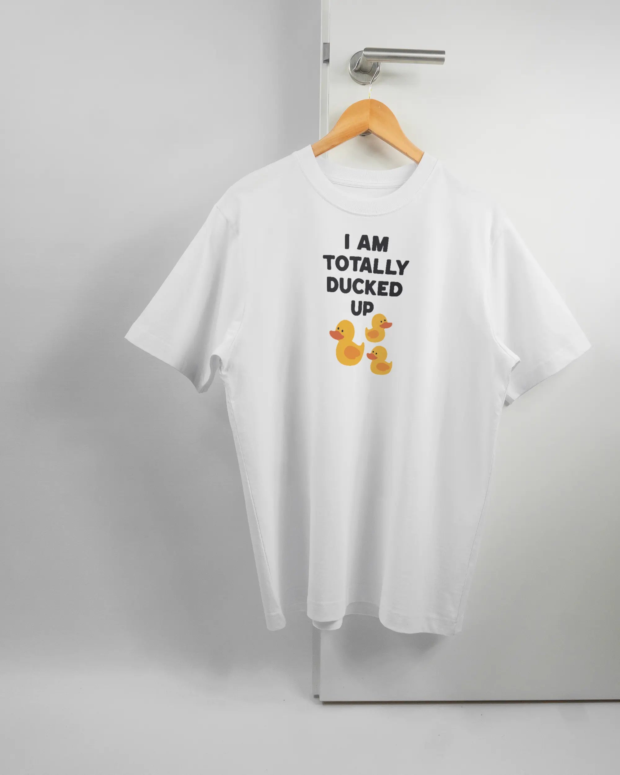 Vorderseite des Organic Unisex T-Shirt Heavy Oversized von Maondo mit dem Design Ducked Up in der Farbe White und in der Größe S auf einem Bügel an der Türklinke aufgehängt