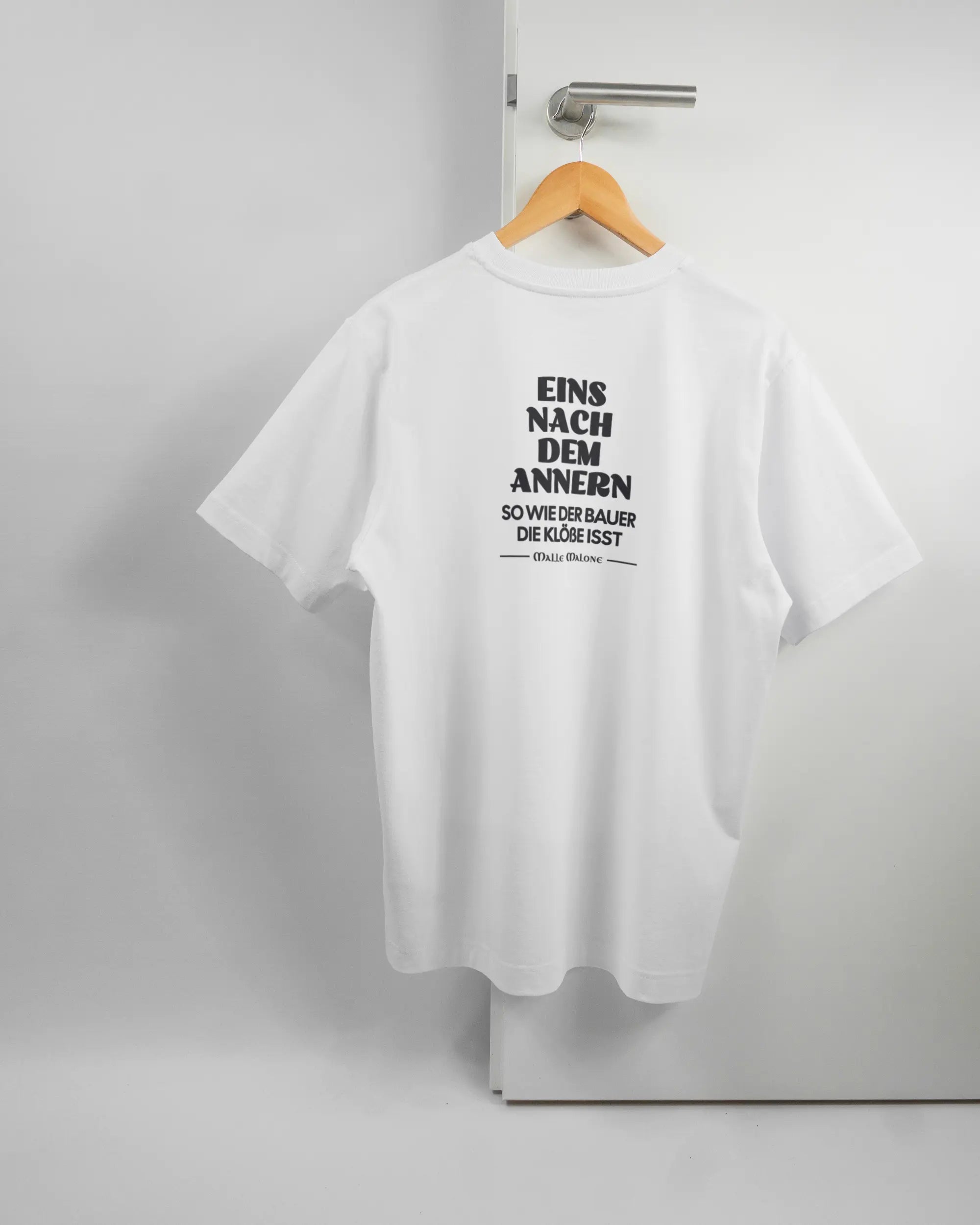 Rückseite des Organic Unisex T-Shirt Heavy Oversized von Maondo mit dem Design Eins nach dem Annern in der Farbe White und in der Größe S auf einem Bügel an der Türklinke aufgehängt