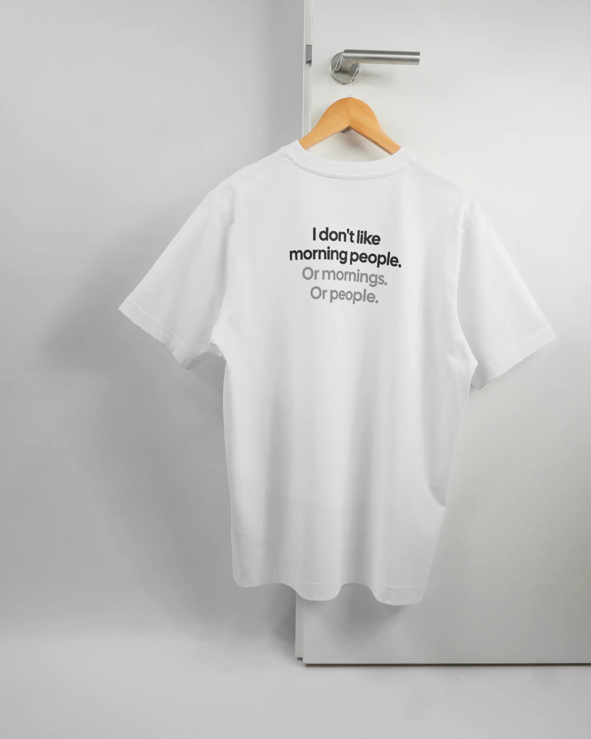 Rückseite des Organic Unisex T-Shirt Heavy Oversized von Maondo mit dem Design Morning Person in der Farbe White und in der Größe S auf einem Bügel an der Türklinke aufgehängt
