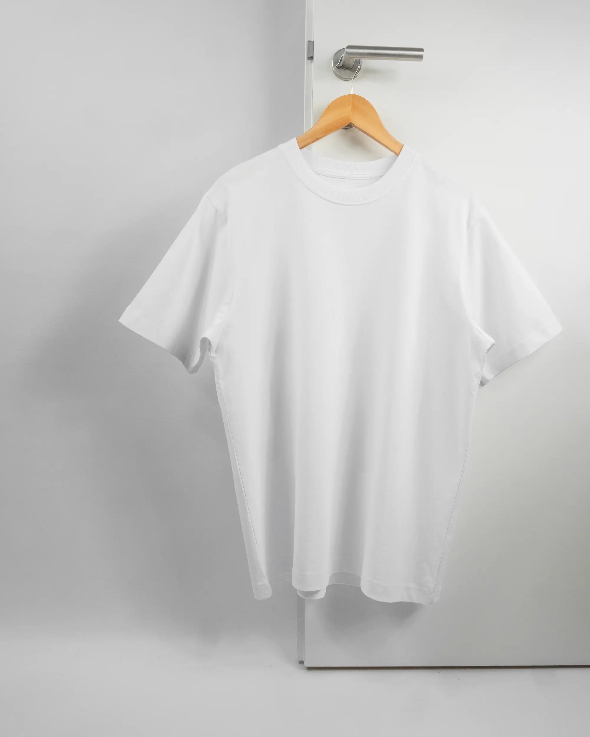 Vorderseite des Organic Unisex T-Shirt Heavy Oversized von Maondo ohne Motiv in der Farbe White und in der Größe S auf einem Bügel an der Türklinke aufgehängt